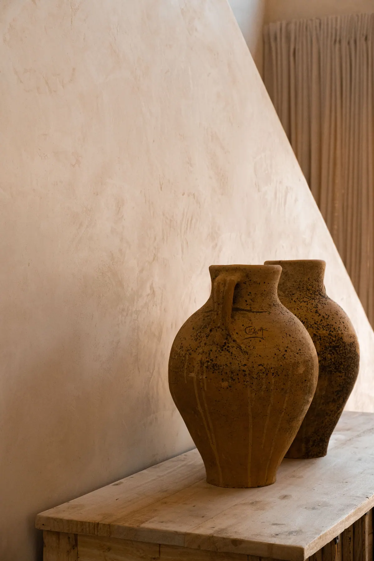 Two terracotta amphorae on a wooden console against a curved lime wall