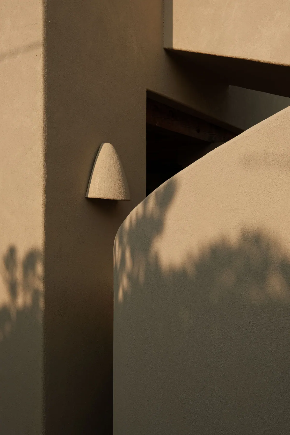 A sculpted wall light on a warm wall with the shadow of leaves