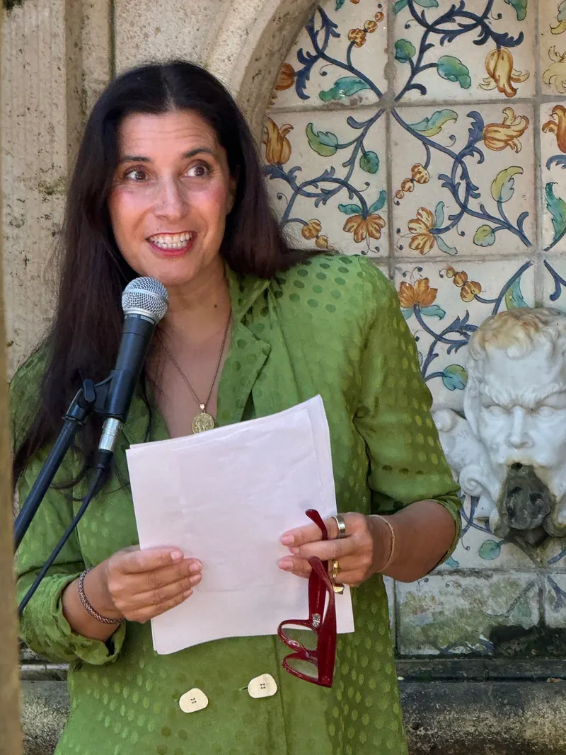 Jessica Bataille speaking at a microphone in front of a tiled fountain
