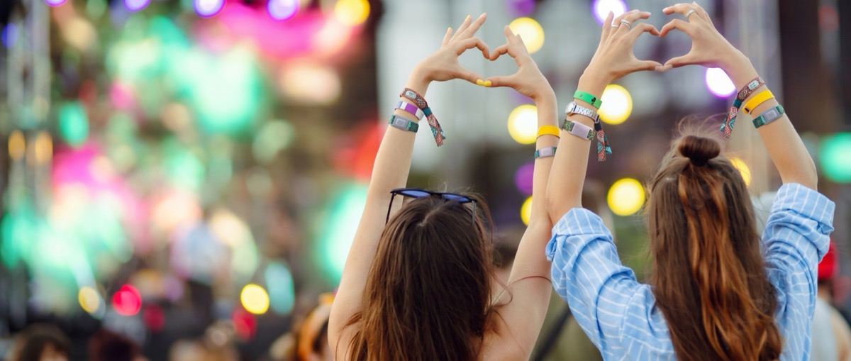 Two friends at a concert raising their hands, several RFID wristbands on their wrists